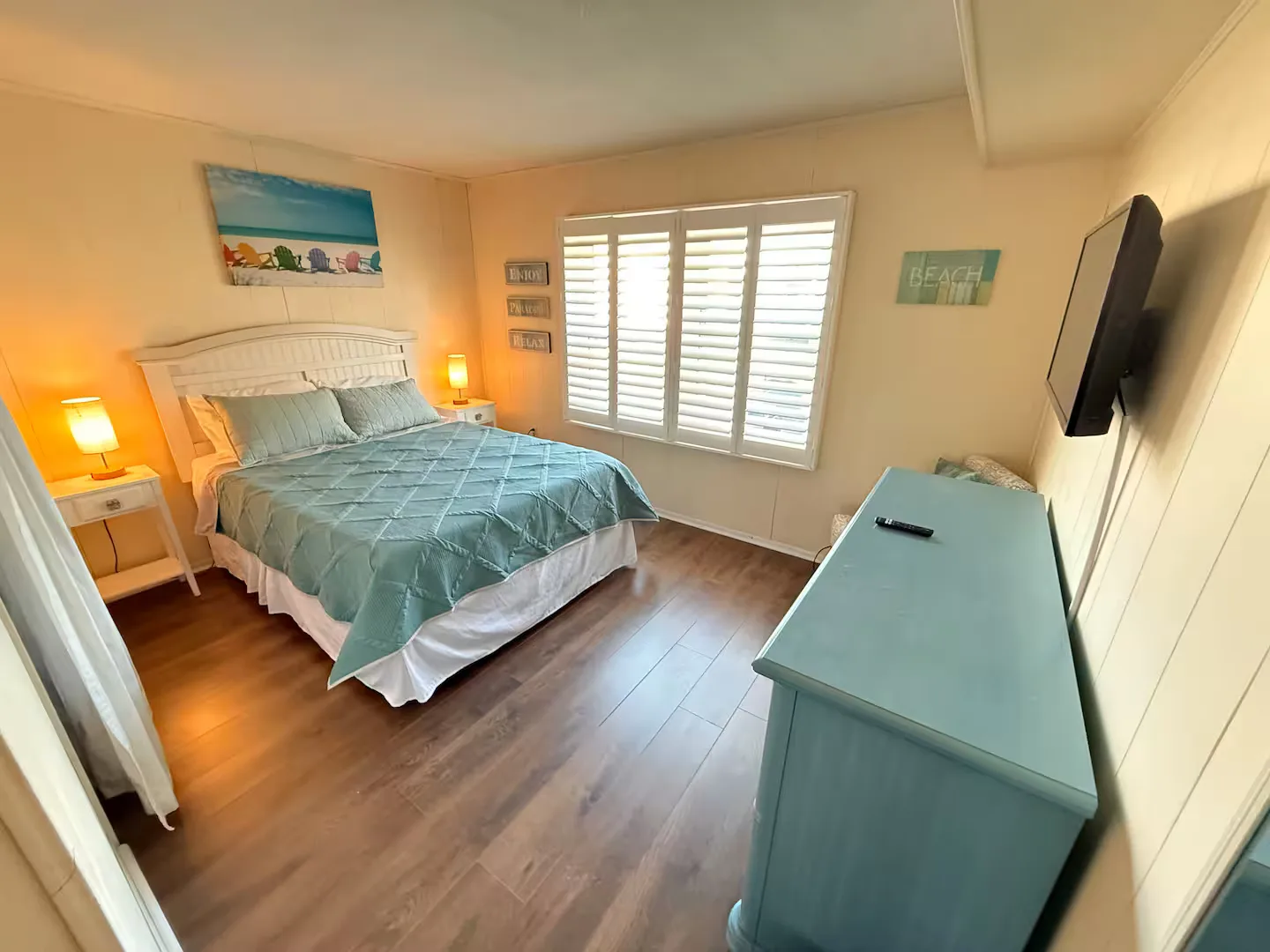 Calm coastal bedroom — plantation shutters and warm lamplight